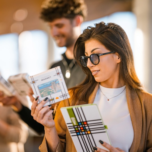 A smiling young woman with sunglasses browsing carefully designed gifts at the Belgrade 360 Deck souvenir shop.